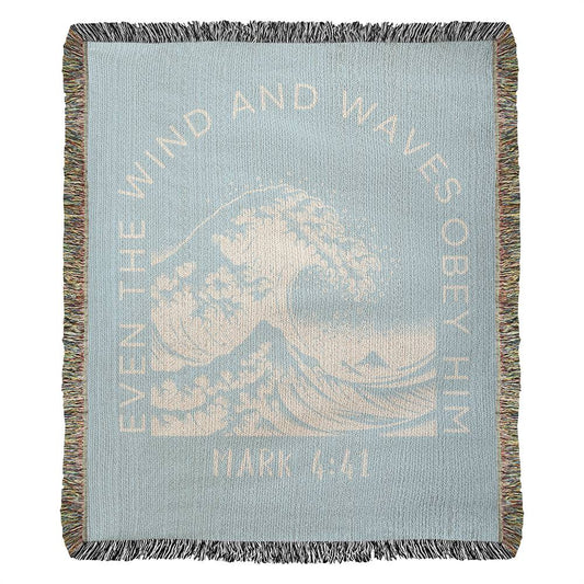 Light blue 100% woven cotton yarn blanket with white text, featuring 'Even the Wind & Waves Obey Him' with ocean wave design and Mark 4:41.
