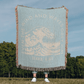 Light blue 100% woven cotton yarn blanket with white text, featuring 'Even the Wind & Waves Obey Him' with ocean wave design and Mark 4:41.
